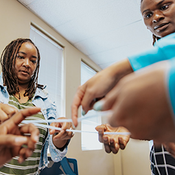 Hands in the foreground pull on strings as two instructors watch.