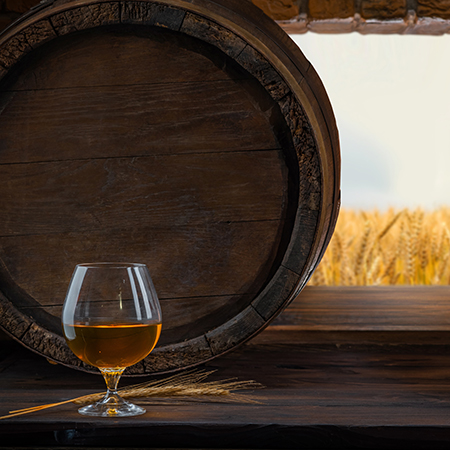 Glass with whiskey, spikelets of wheat, brandy on a vintage background of a rustic oaken barrel.
