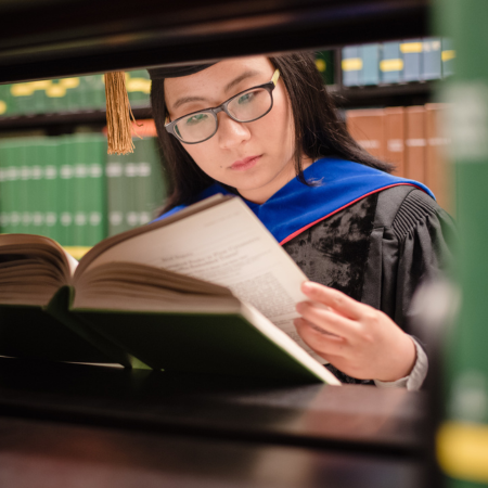 Student in Ph.D. graduation robes reading a book