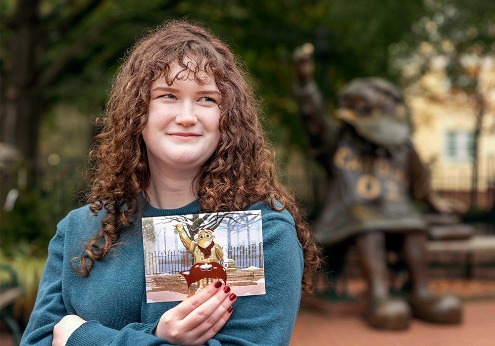 Audrey Webb holds a copy of her winning artwork as she stands in front of the Cocky statue