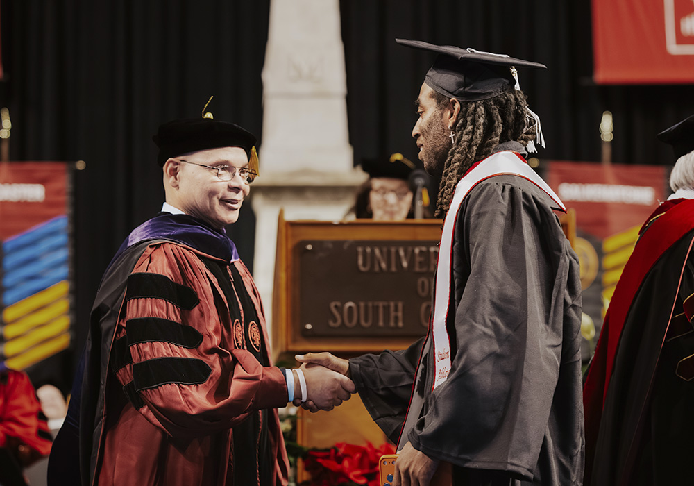 A graduating student shakes an official's hand on stage.