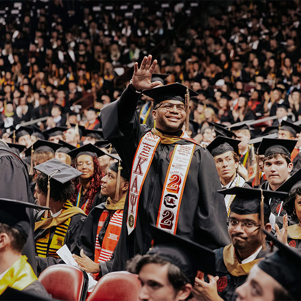 student stands and waves at commencement ceremony