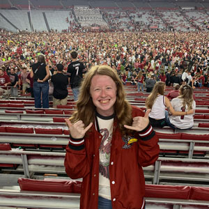 woman standing in a football stadium giving the "spurs up" hand sign