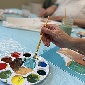 A hand dabs a brush into a palette of paint.
