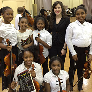 A group of female students holding stringed instruments and their instructors
